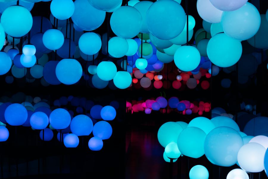 Hundreds of glowing spheres in cyan and red hanging in a dark hall.