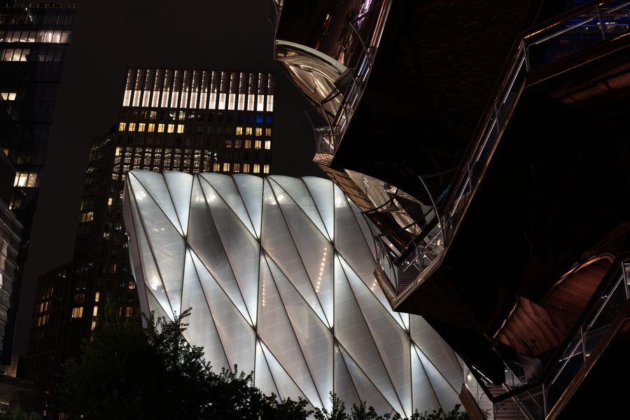 The faceted white shell of the Shed against dark towers.